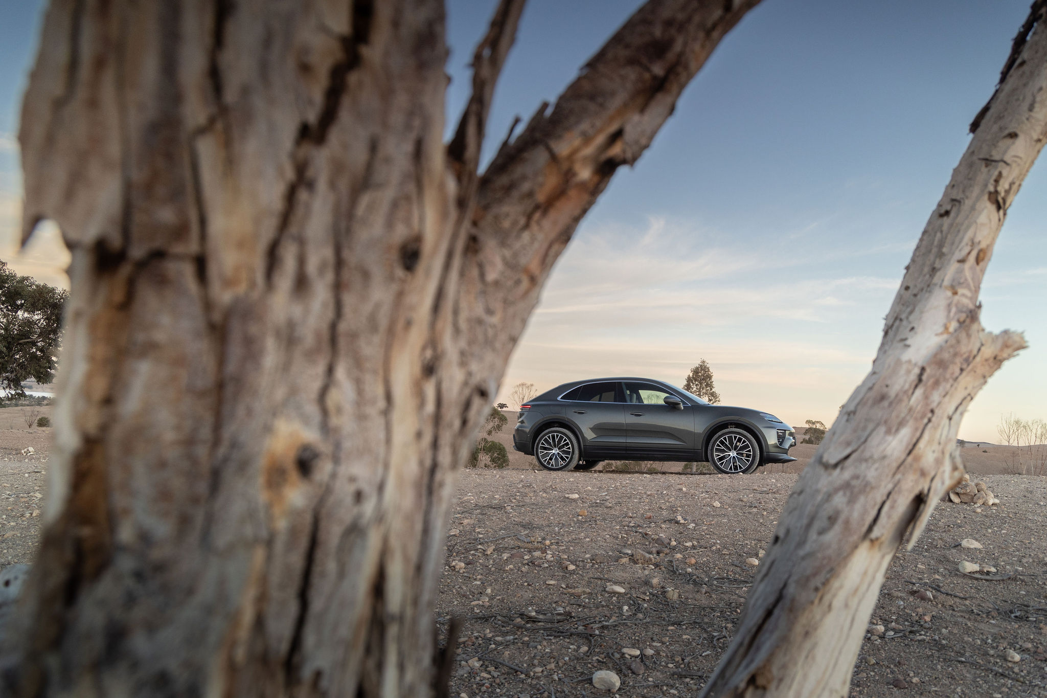 Porsche Macan Électrique dans le désert d’Agafay Porsche Macan électrique en arrière-plan vu à travers un arbre dans le désert d’Agafay