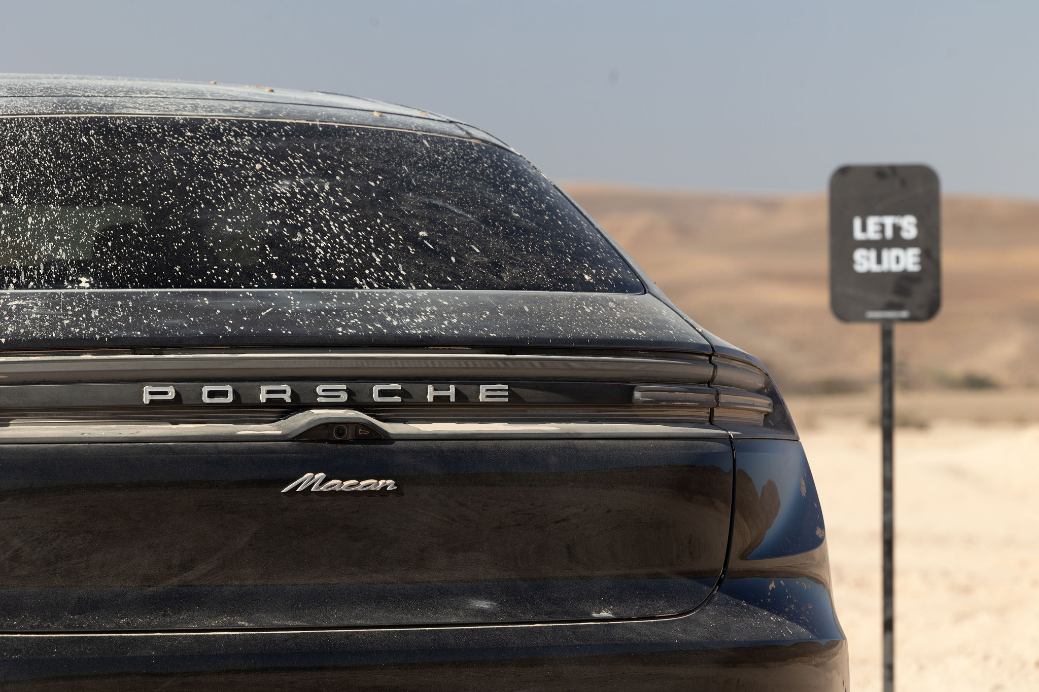 Vue arrière du Porsche Macan Électrique dans le désert d'Agafay Vue arrière du Porsche Macan électrique avec le panneau "Let's Slide" dans le désert d'Agafay