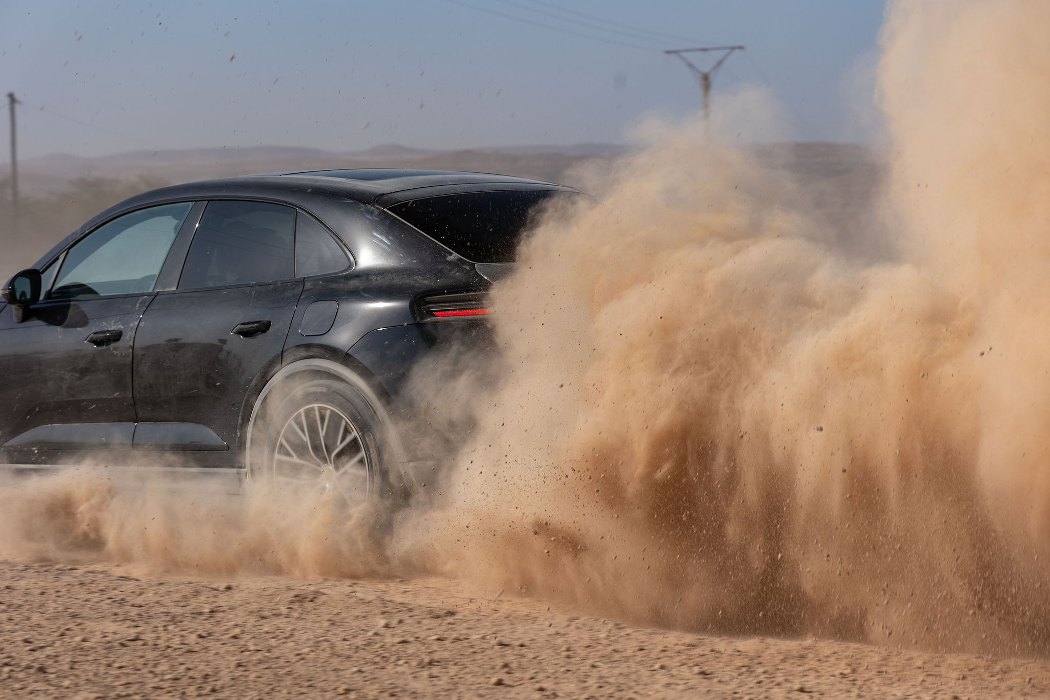 Porsche Macan Électrique et nuage de poussière dans le désert d’Agafay Porsche Macan électrique soulevant un nuage de poussière dans le désert d’Agafay